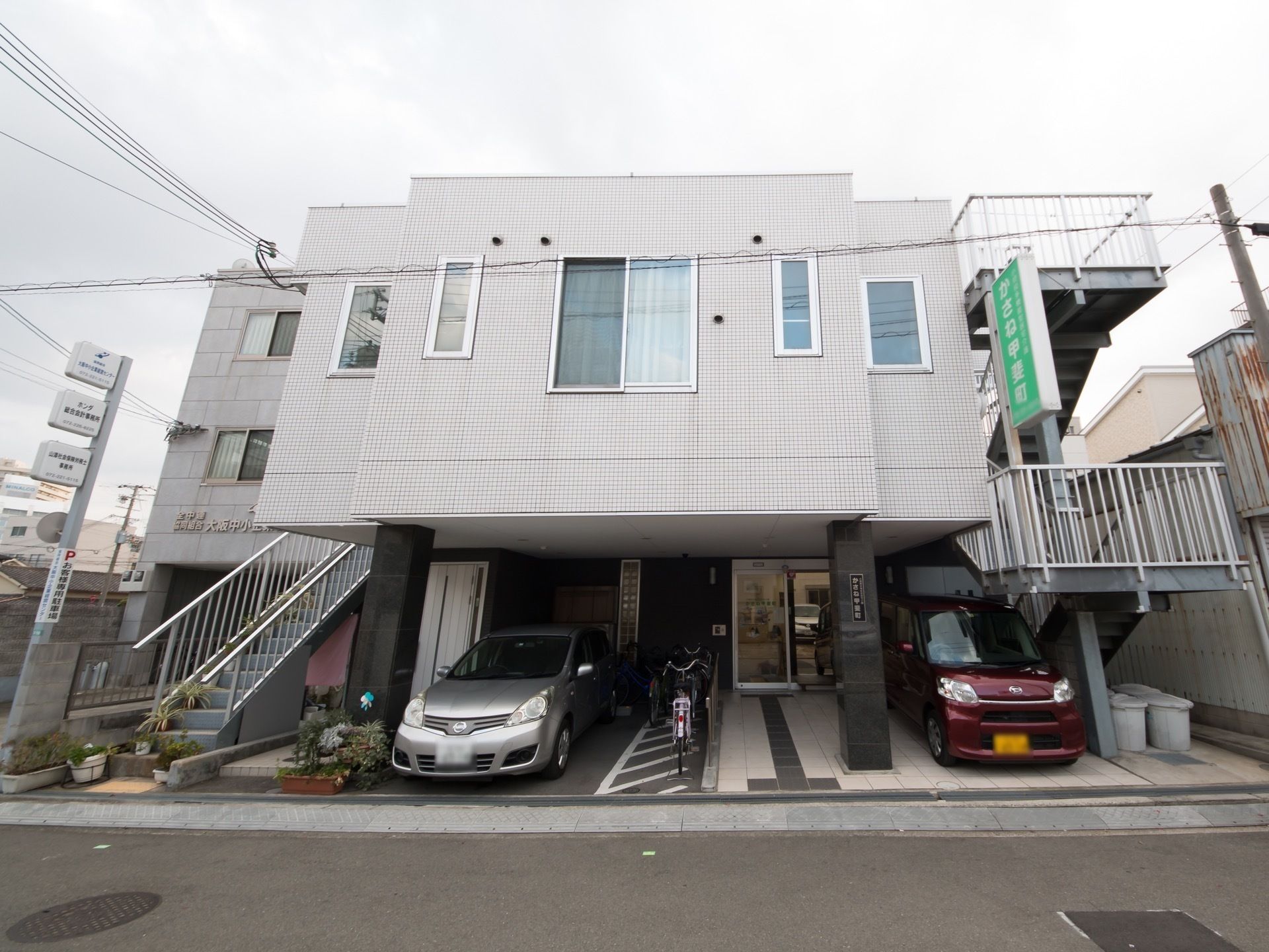 白い建物は屋外に避難用の階段が付き、1階部分に駐車場もある。
