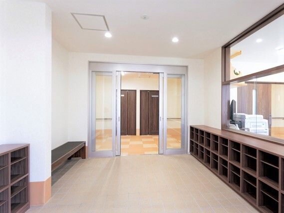 背の低いブラウンの靴箱が玄関の両サイドにあり、自動ドアの近くにはベンチも置かれている。