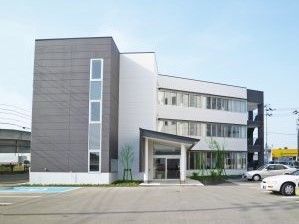 青空が広がる写真。手前に駐車場スペースがあり鉄骨造の建物が奥に写っている