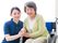 車椅子に座って微笑む高齢女性と隣に寄り添う女性ヘルパー