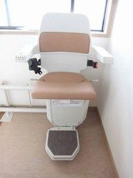 階段昇降機が設置されている。シートベルトが付いた白とベージュの椅子の両サイドに肘置きがある。