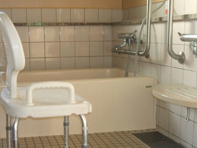 白いタイルが貼られた浴室には一人用の浴槽とシャワー、シャワーチェアなどが置かれている。