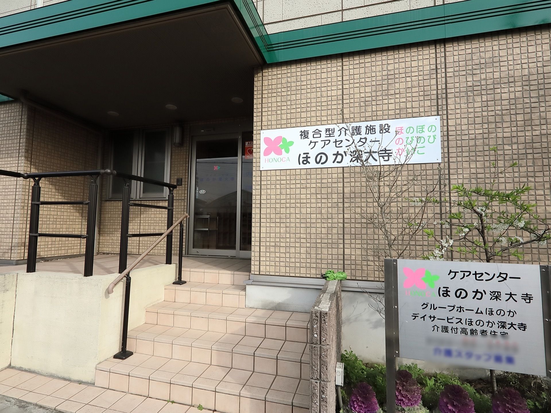 大きな屋根を持つ玄関ポーチには階段とスロープが設置されており、それぞれに手すりが用意されている。その脇には施設の案内板が置かれている。