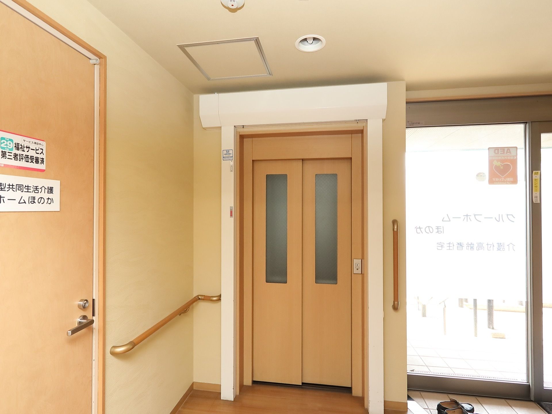 エレベーターは玄関のすぐ左手に設置されている。外扉は他の建具に馴染む木調のデザインである。操作スイッチは右手についている。