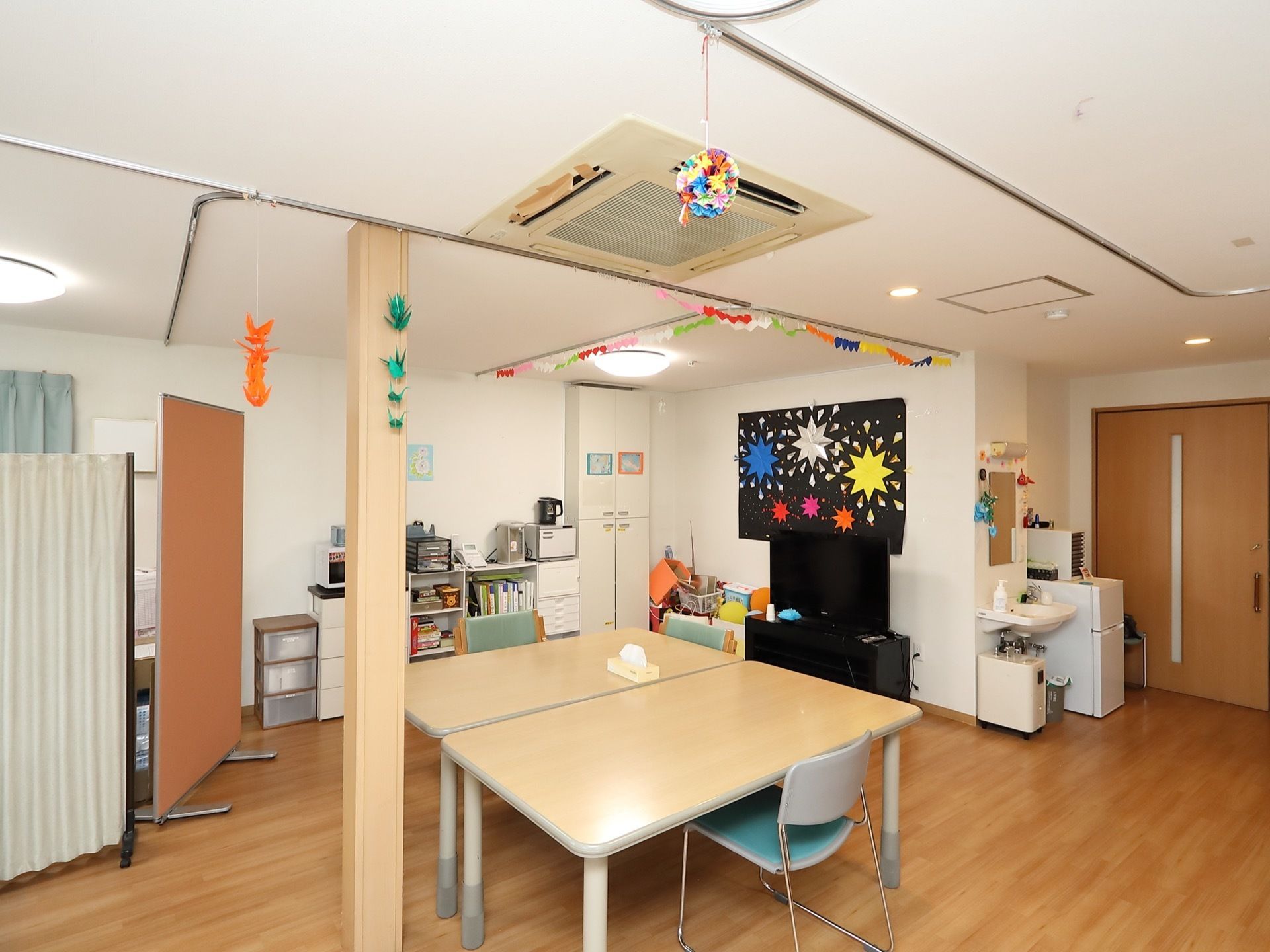 天井から折り紙細工が提げられている広間。液晶テレビの後ろの壁面には、躍動感のある大きな平面作品が展示されている。