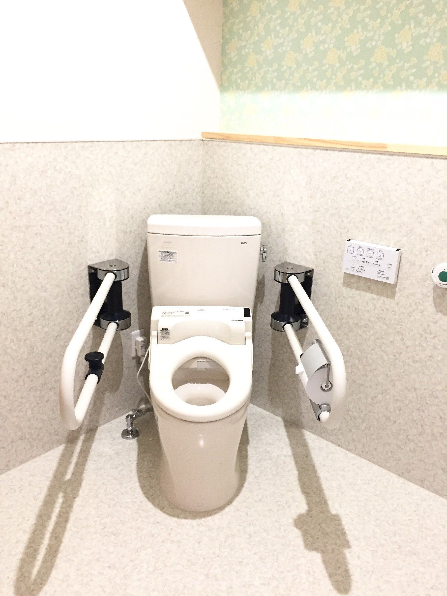 両サイドに手すりが付いたトイレにふたはなく、壁には操作パネルと呼び出しボタンがある。