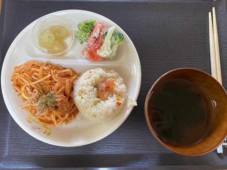 トマトソースのスパゲッティやピラフ、サラダ、皮をむいたぶどうなどがワンプレートに盛られている。