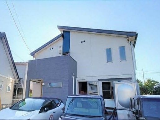 住宅地の中にある２階建ての建物の前には駐車場があり、車が止まっている。