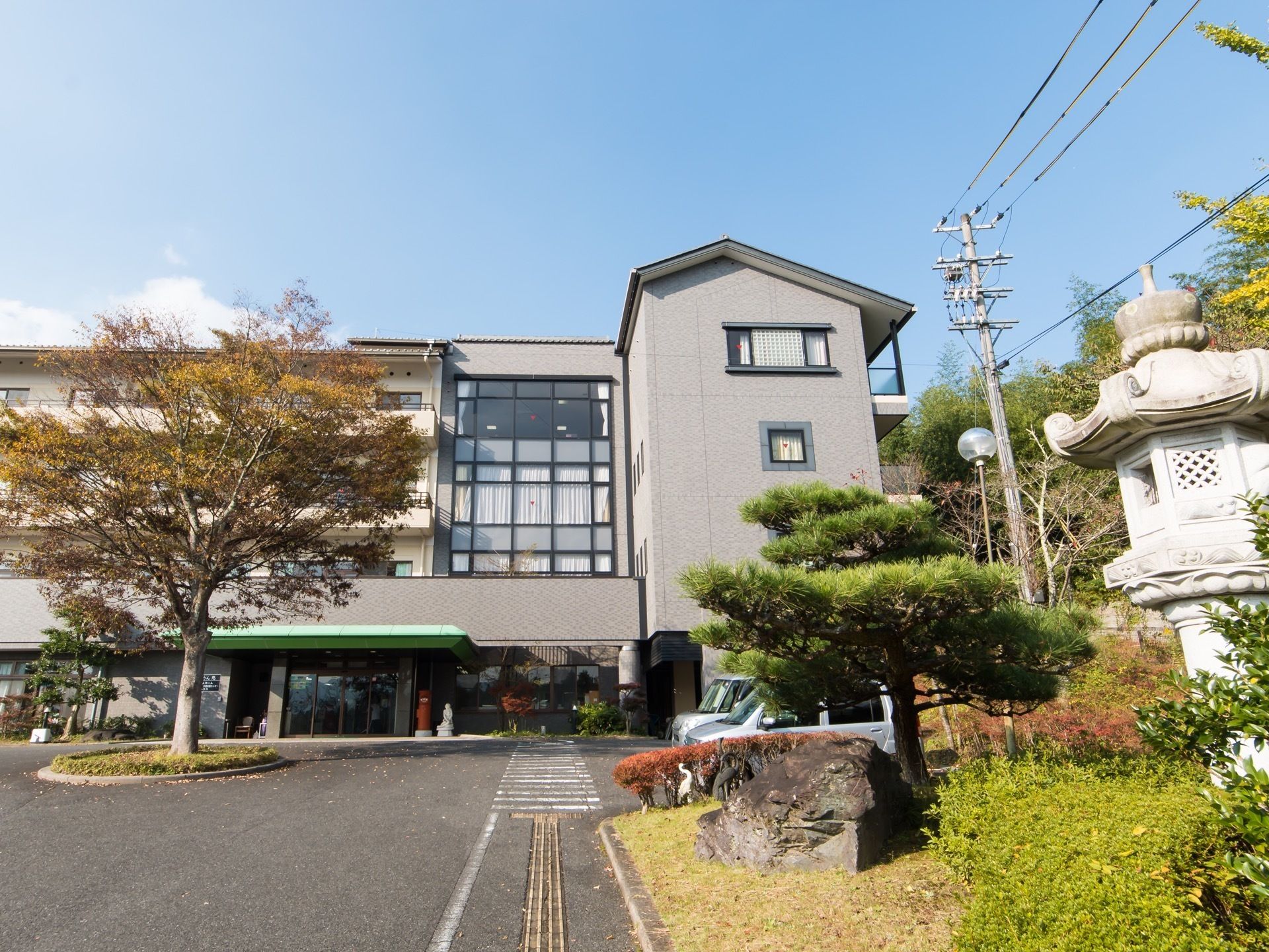 落ち着いた色調の外壁を持つ４階建ての施設である。玄関前には薄緑色の大きなひさしがある。植栽の中に大きな灯籠が立てられている。