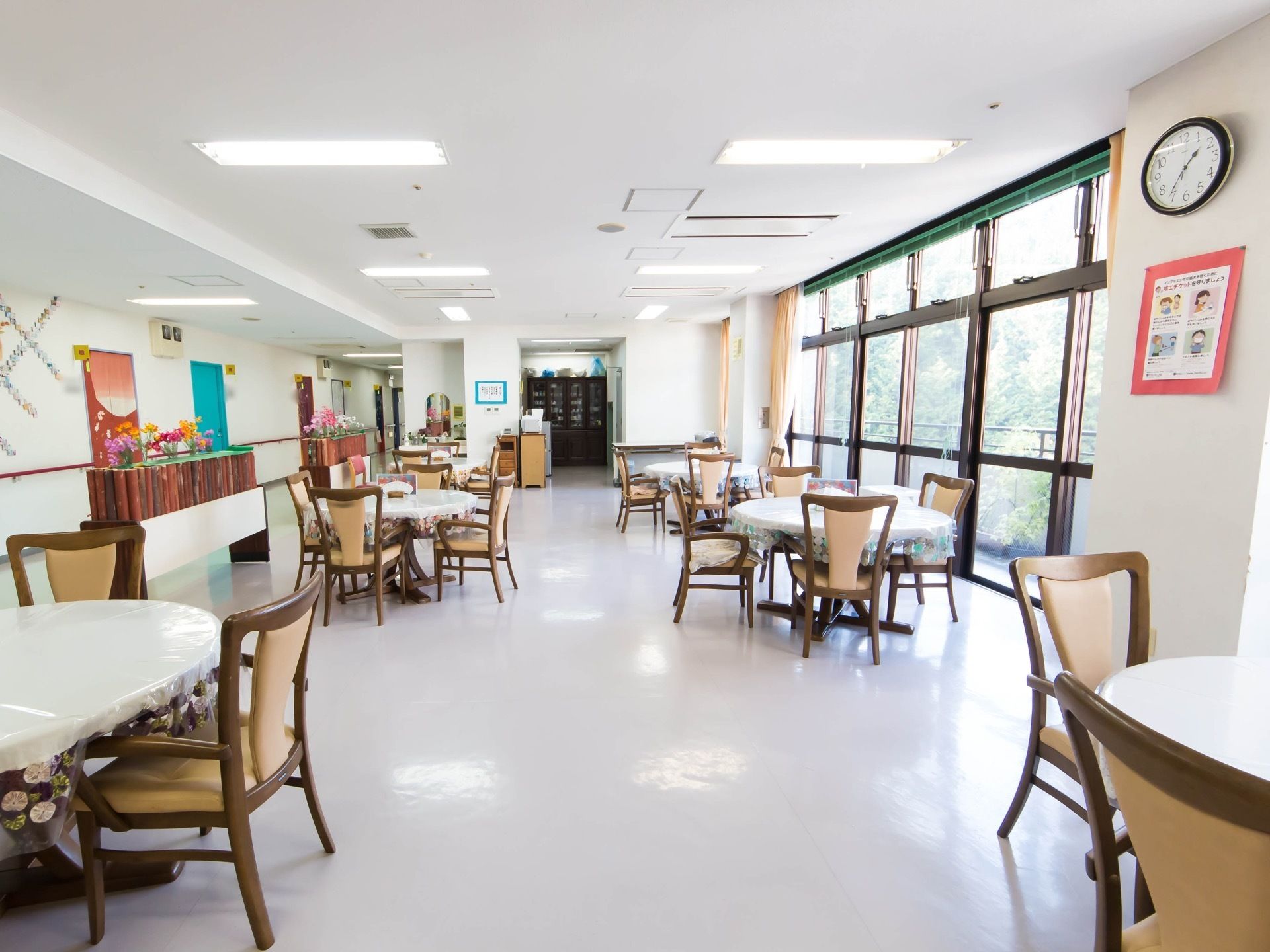 広々とした食堂である。大きな窓からの採光や照明で明るい雰囲気。丸テーブルと背もたれつきの椅子が多く置かれている。