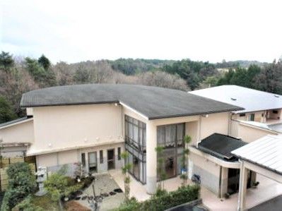 自然に囲まれた環境の中にたたずむ2階建ての建物。グレーの屋根に白い壁。