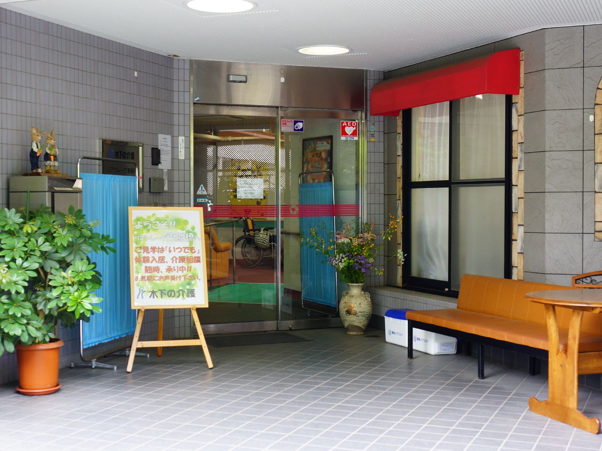 建物の入り口は自動ドアであり、その奥の段差もスロープがあるので、車いすの方でも建物内に入りやすい。また、ドア付近にはベンチもある。