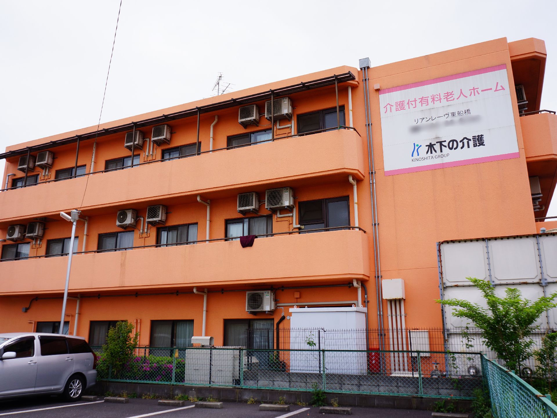 4階建ての建物でオレンジ色をしている。各部屋にバルコニーがあり、それぞれ室外機が設置されている。右側には大きな看板がつけられている。