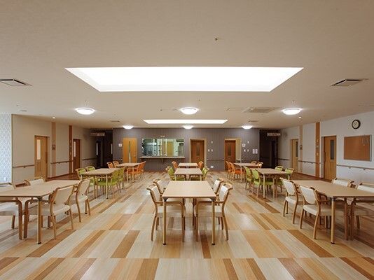 木製のダイニングテーブルが複数置かれ、ぬくもりが感じられる明るい食堂。厨房がすぐそばにある。