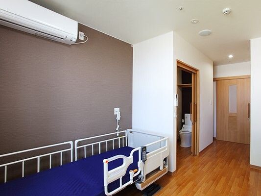 エアコンが付いたシンプルな居室。壁には緊急通報装置が付き、トイレは引き戸。