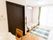 スライド式のドアが付いたトイレが設置されたフローリングの部屋。ラグや寝具付きのベッド、カーテンなどが付いている。