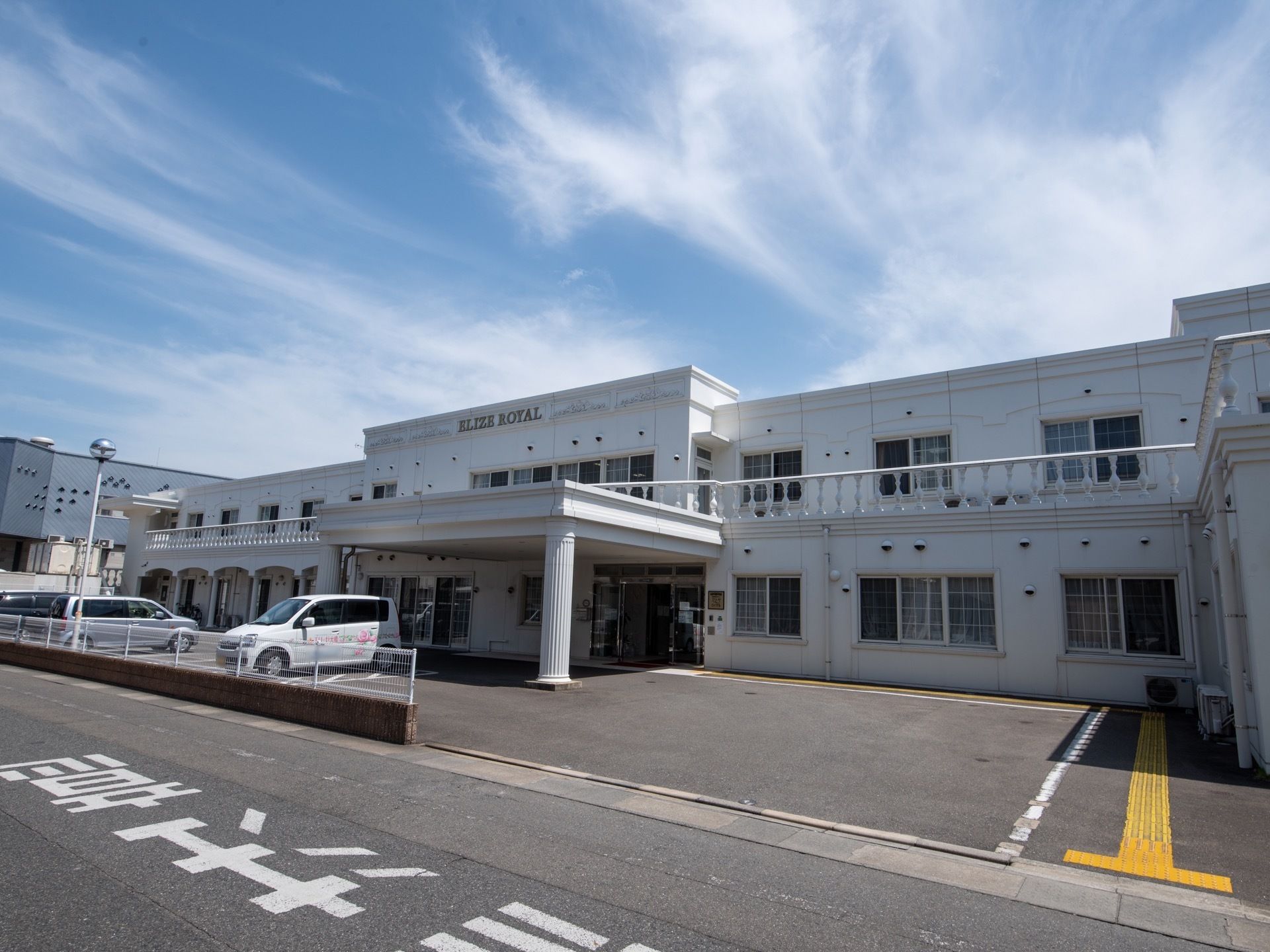 2階建てのヨーロッパ調の大きな建物がある。一階の玄関部分には大きなフールが付いている。建物前面は駐車場になっており、車が数台停まっている。
