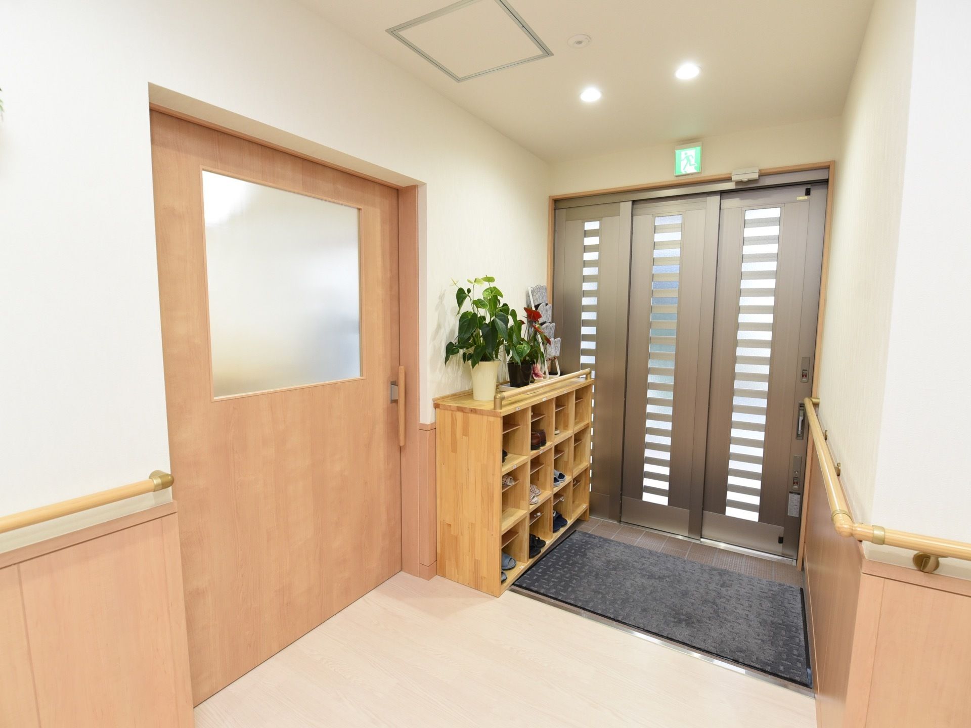 淡いベージュの木目調であたたかみのあるエントランスである。下駄箱が設置され、床には大きなマットが敷かれている。
