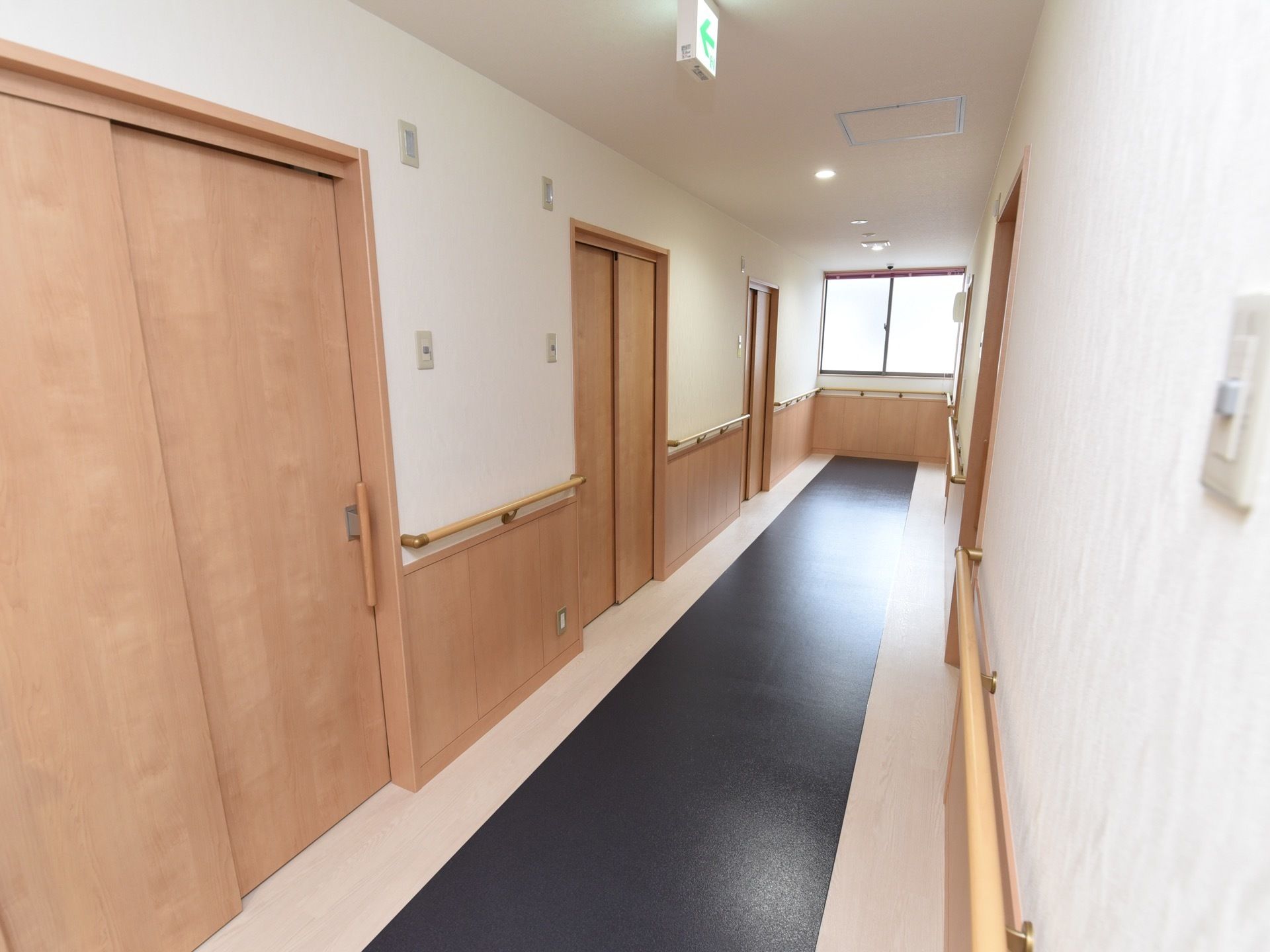 白と淡いベージュの木目のコントラストがあたたかみを与える廊下である。居室の入口は引き戸で、にぎりやすい取っ手がついている。