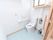 窓から日差しが射し込んでいる広いトイレである。ナースコールや手すりが備わっている。新聞紙を切ったものとゴミ箱が置かれている。