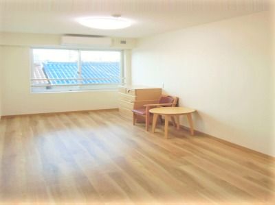 落ち着いた色合いのフローリング仕様の床と木星の家具がある部屋。奥のほうにエアコンと窓がある様子