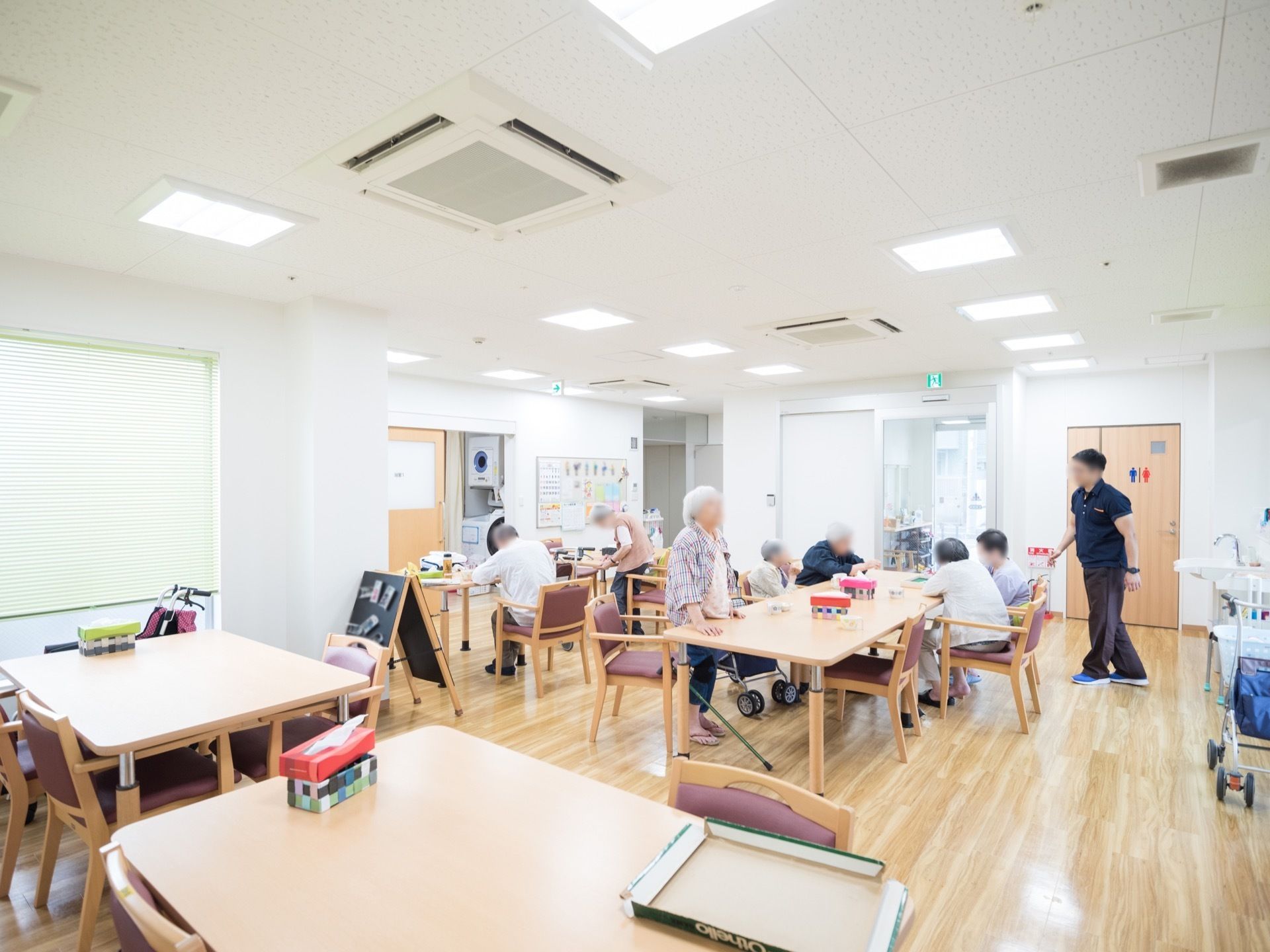 四角のテーブルが複数並べて置かれており、そのまわりには背もたれ付きの椅子がある。テーブルの上にはティッシュの箱が置いてある。