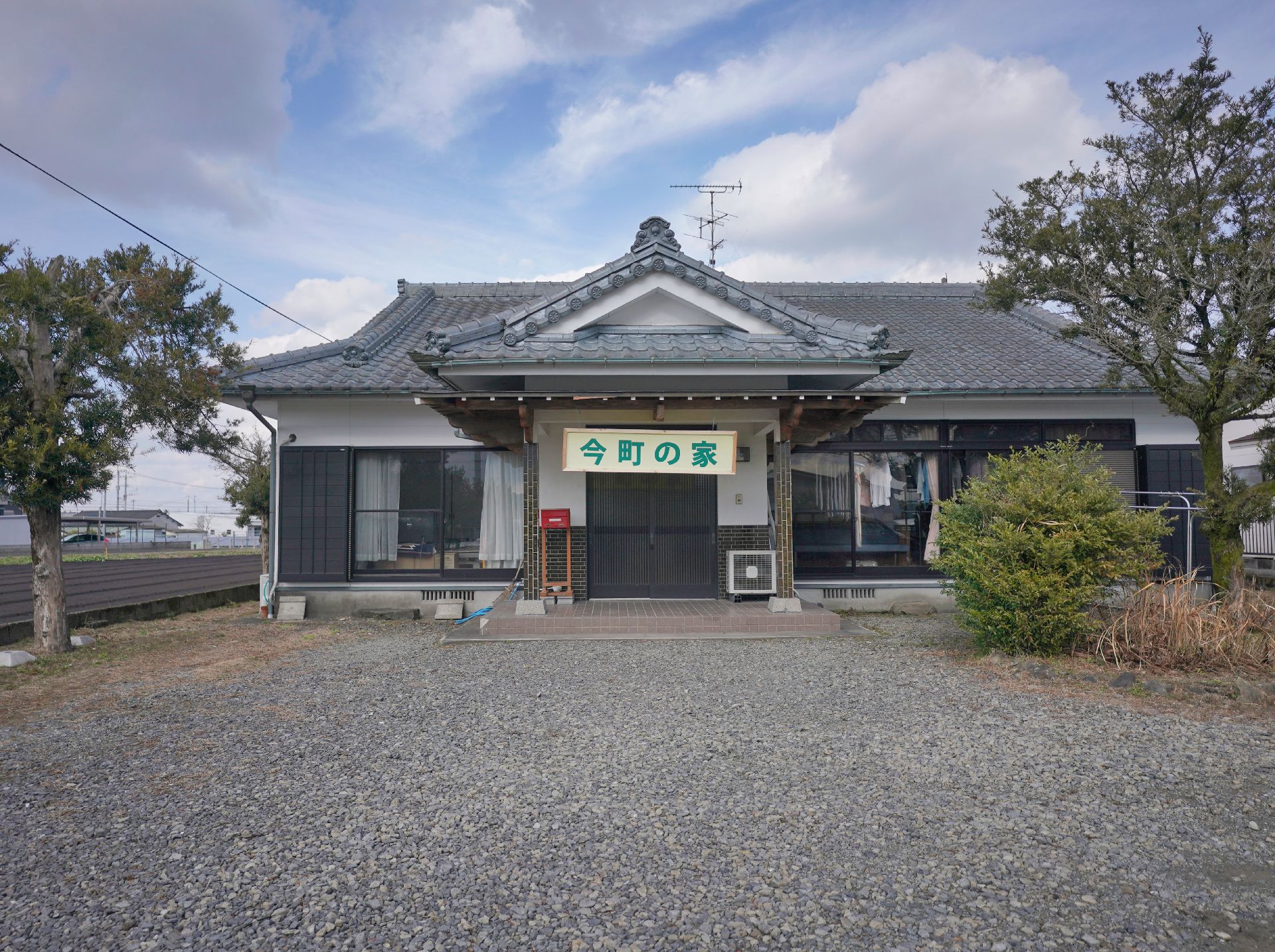 シャツを着た高齢男性が笑顔で福祉車両から降りようしていて、若いスタッフが手伝っている。