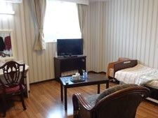 寝具付きのベッドが置かれたフローリングの部屋にはデスクセットやテレビが置かれ、車いす対応の洗面所がある。
