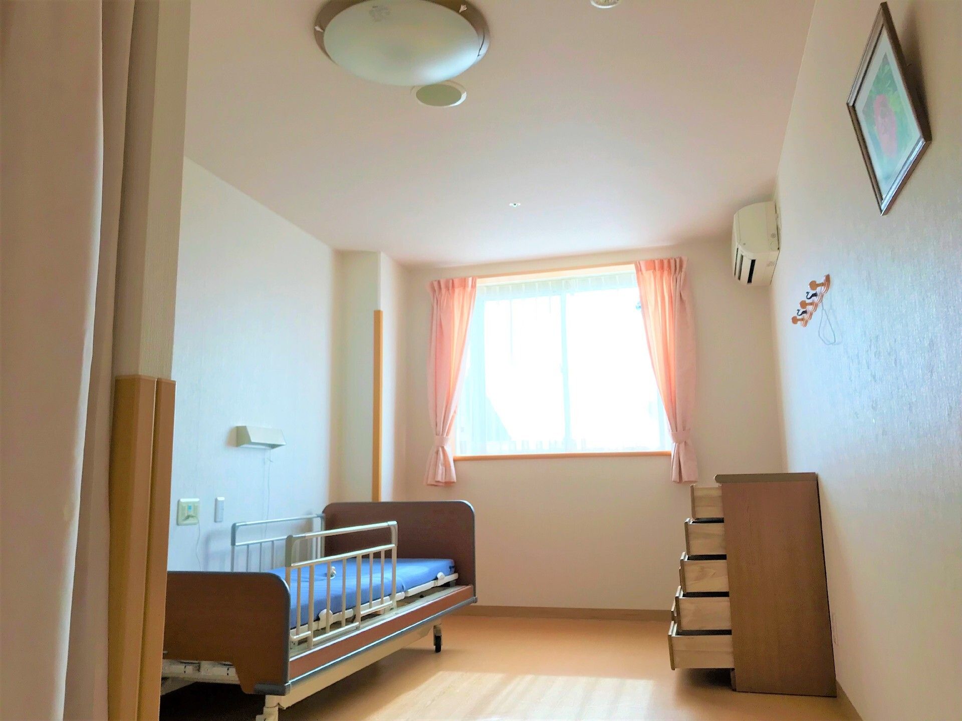 シングルベッドと窓がある小さなワンルームタイプの部屋の様子。施設内の居室