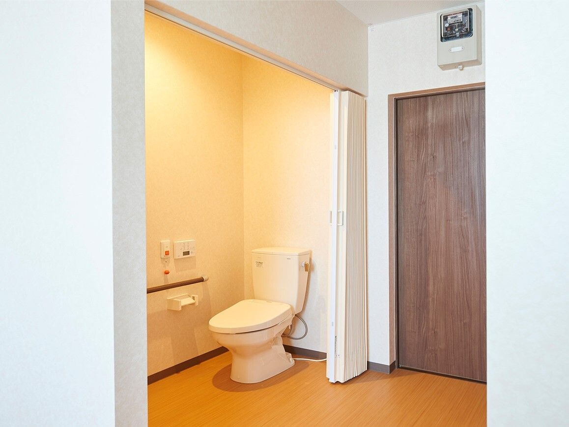 トイレには呼び出しボタンや手すりが付き、アコーディオンカーテンが設置されている。