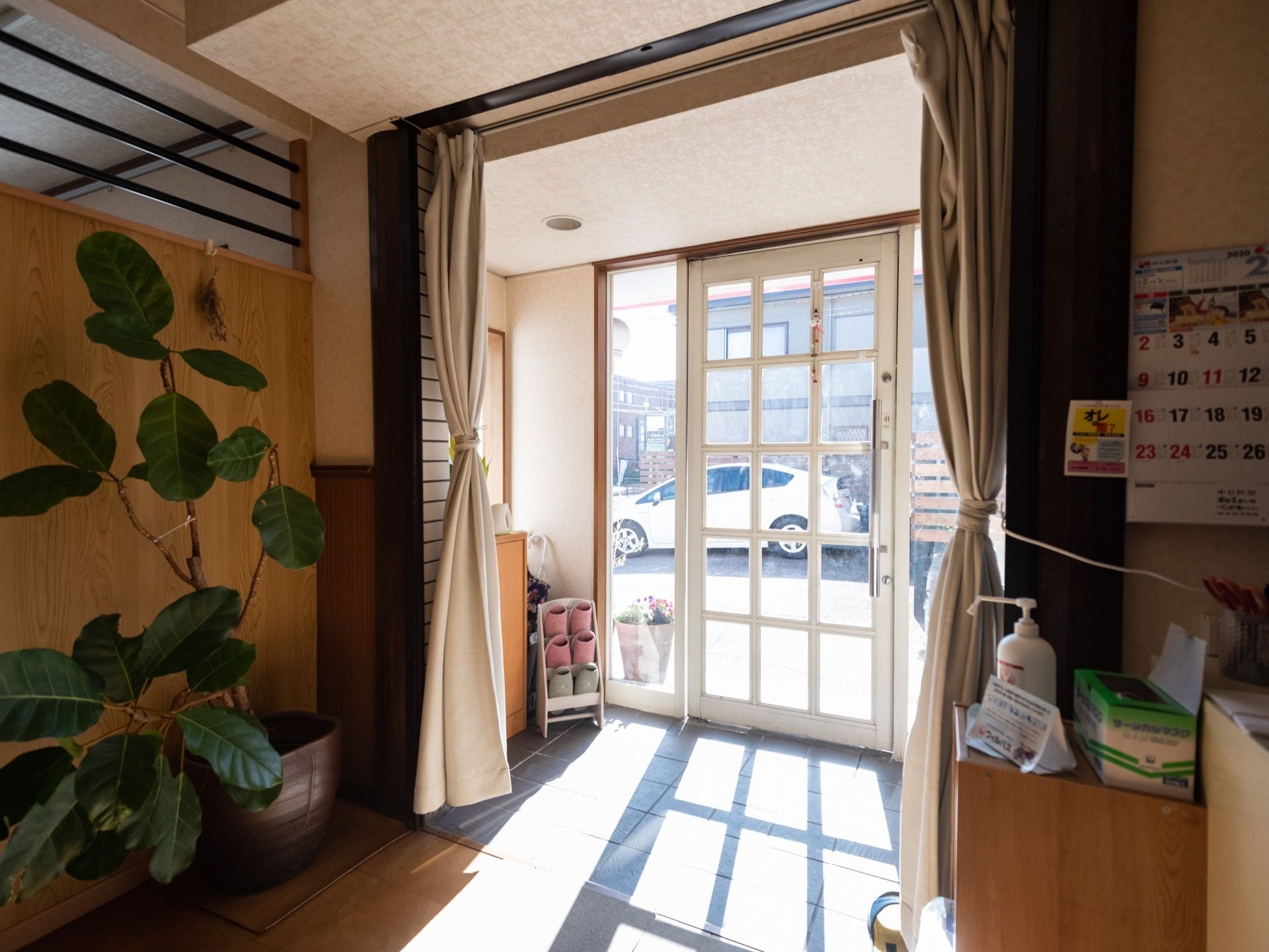 エントランスには傘立てがあって、スリッパを用意している。手前の通路には、大きな観葉植物が飾られている。