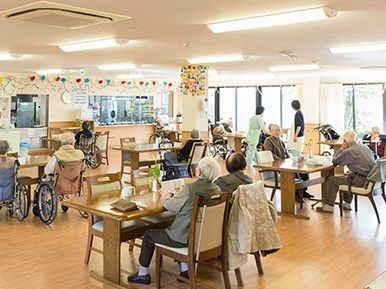 大勢の入居者でにぎわう食堂。木製のテーブルが複数置かれ、厨房はオープンとなっている。