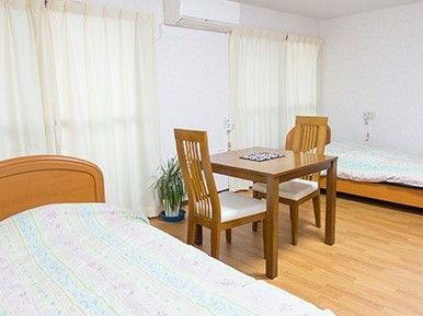 ベッドが二つ、ダイニングテーブルなどの家具とエアコンが設置された居室には緊急通報装置も設置されている。