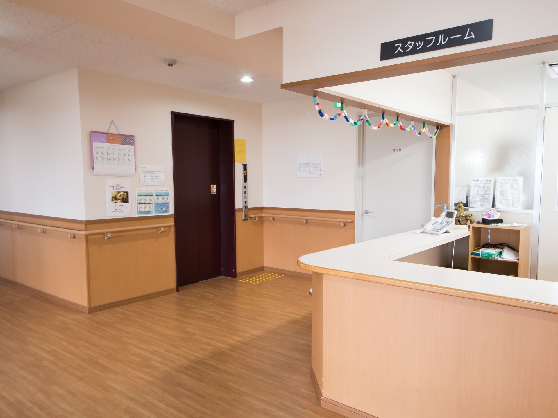 スタッフルームはオープンな造りになっている。カウンターには電話機が置かれている。すぐ目の前にエレベーターの乗降口がある。
