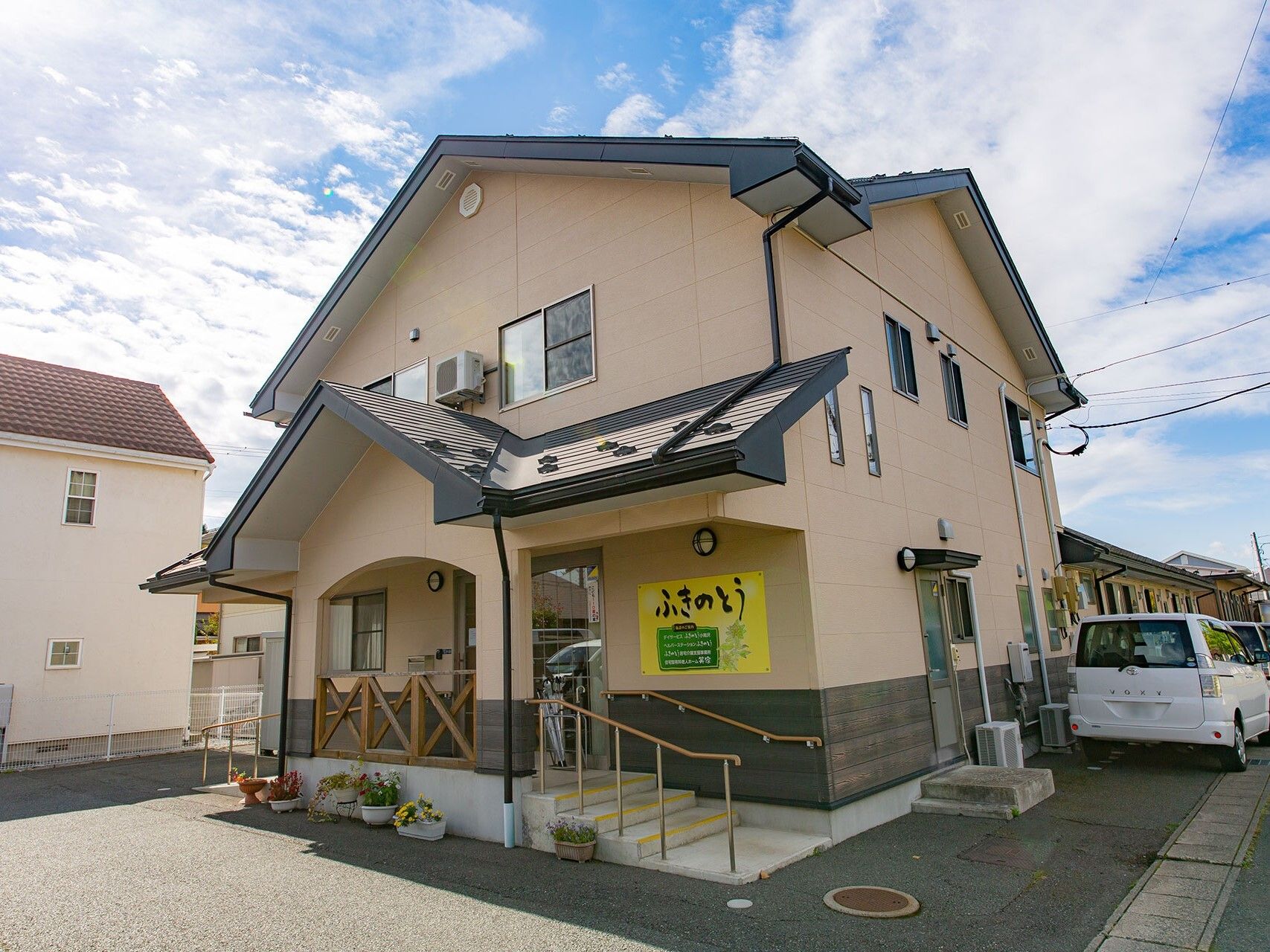 ２階建ての建物は日当たり良好で建物の玄関には手すり付きの階段や屋根があり、車が止まるスペースもある。