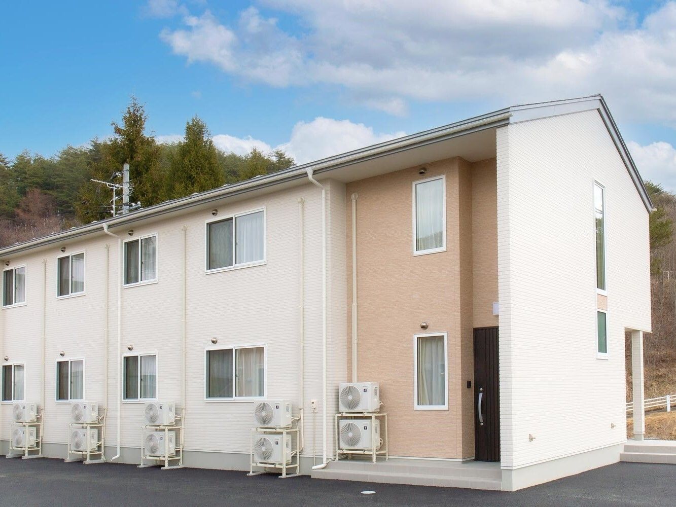 白とベージュの2階建ての建物は緑に囲まれていて、三角屋根が付き、窓もたくさんある。
