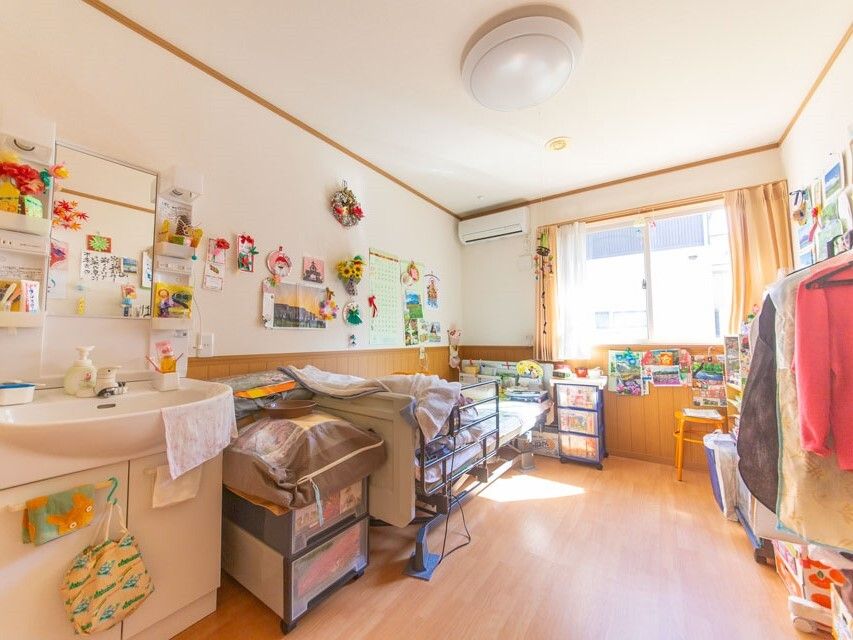 大きな窓が付いたフローリングの居室には寝具付きのベッド屋洗面所、ハンガーラックなどが置かれている。