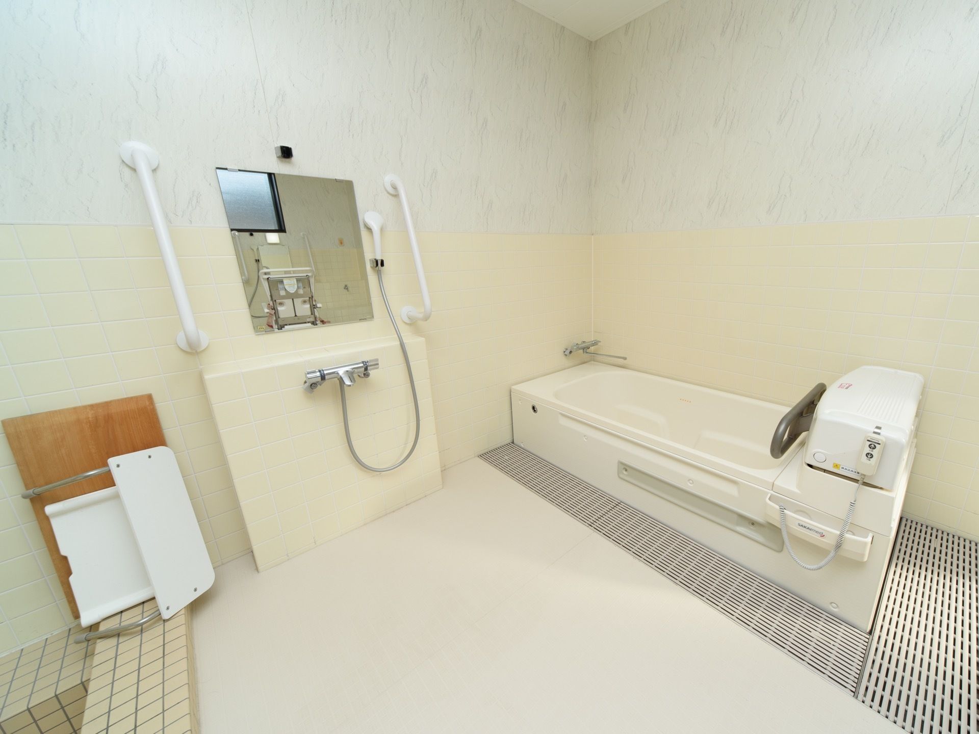 白で統一された浴室の奥には、専用の機械浴槽が配備されている。洗い場の壁には、左右に手すりが取り付けてある。