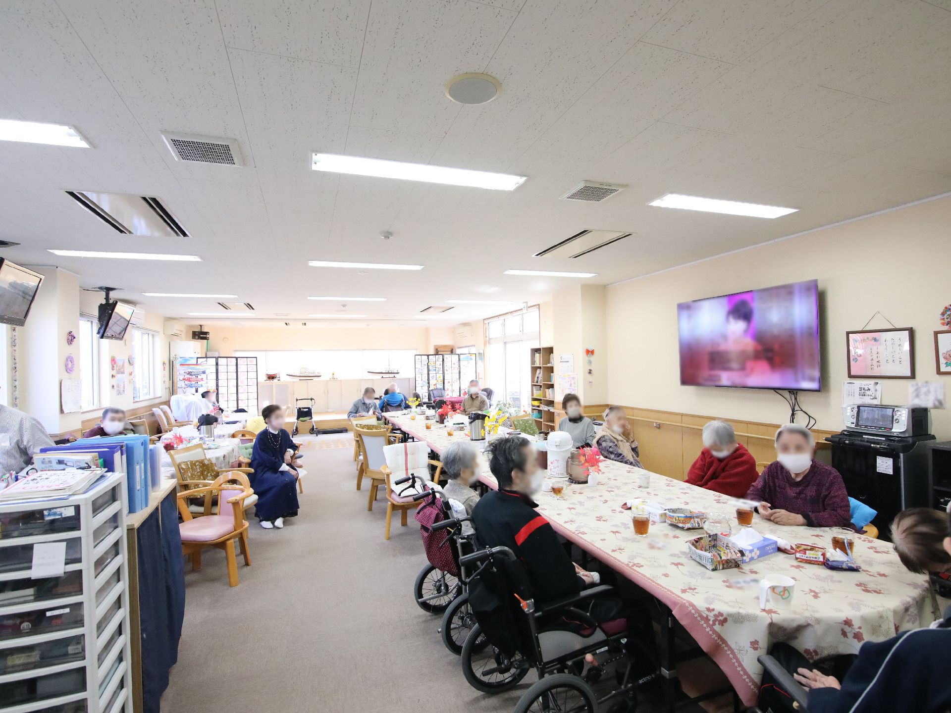 木製のテーブルを囲んで笑顔で話している眼鏡をかけた高齢女性とポロシャツを着た女性スタッフ。