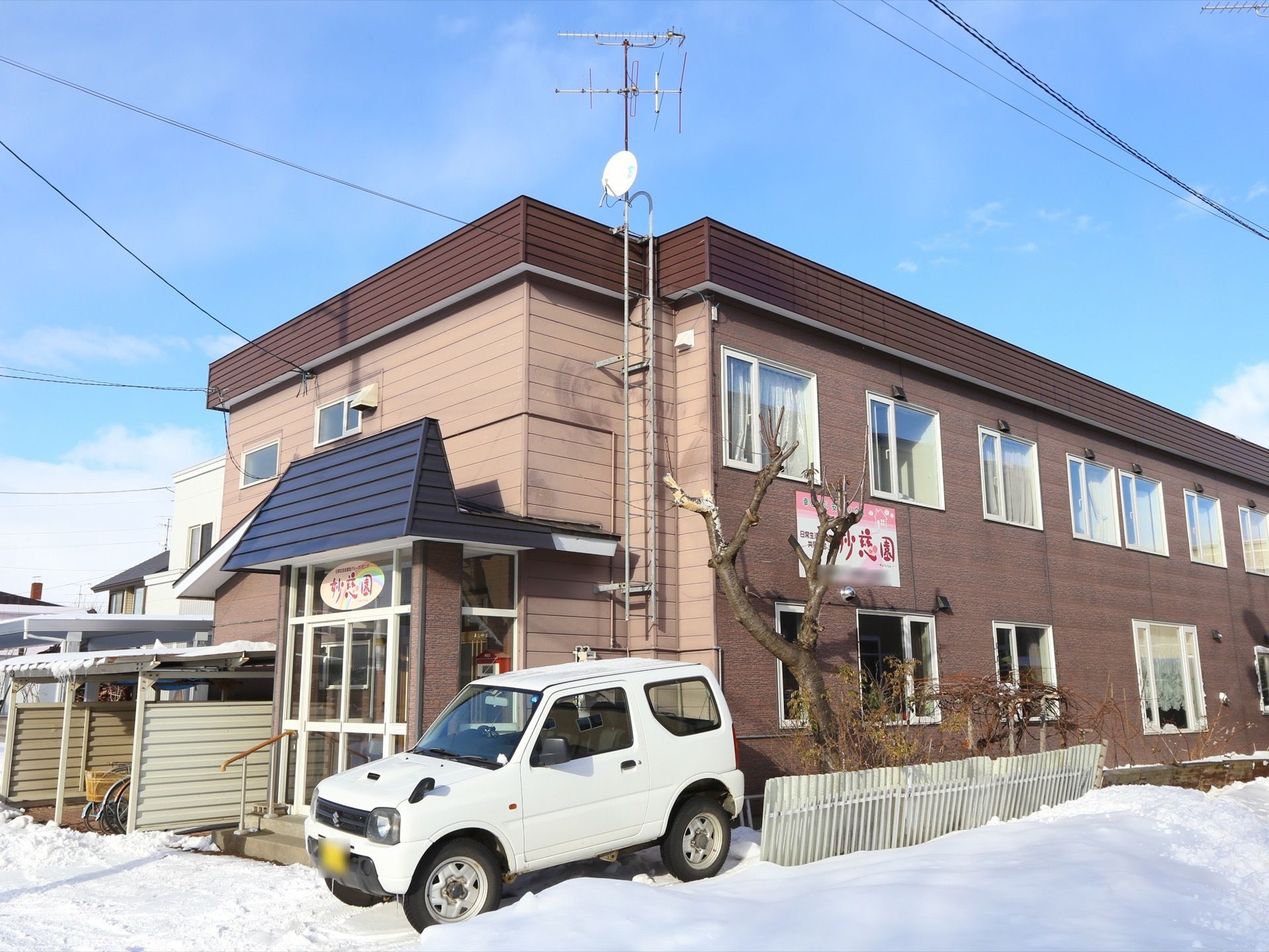 エントランスのそばに駐車スペースと駐輪スペースが設置されている。エントランスは雪国特融のガラスの２重ドアが取り付けられている。