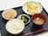 黒いトレーには、卵料理と大根と野菜の煮物、小鉢にはわかめ料理の添え物、みそ汁と白いご飯が並び、手前に箸が置いてある。