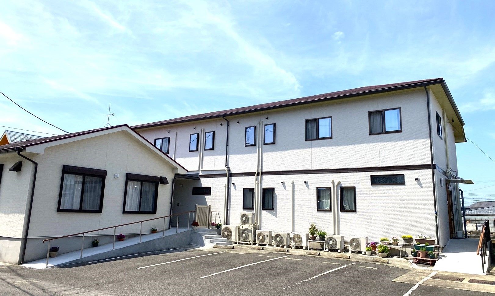 2階建ての建物は黄色と緑の外壁で、オレンジのベランダが付き、敷地内には平屋建ての建物もある。