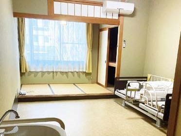 ブルーのユニフォームを着た男性スタッフと白い服を着た高齢女性が並んで体操をしている。