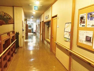 白い服を着た高齢女性とブルーのユニフォームを着た男性スタッフが、笑顔で体操をしている。
