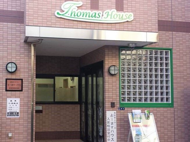 白髪の女性がベッドに横になり、笑顔で花柄のエプロン姿の女性スタッフと話している。