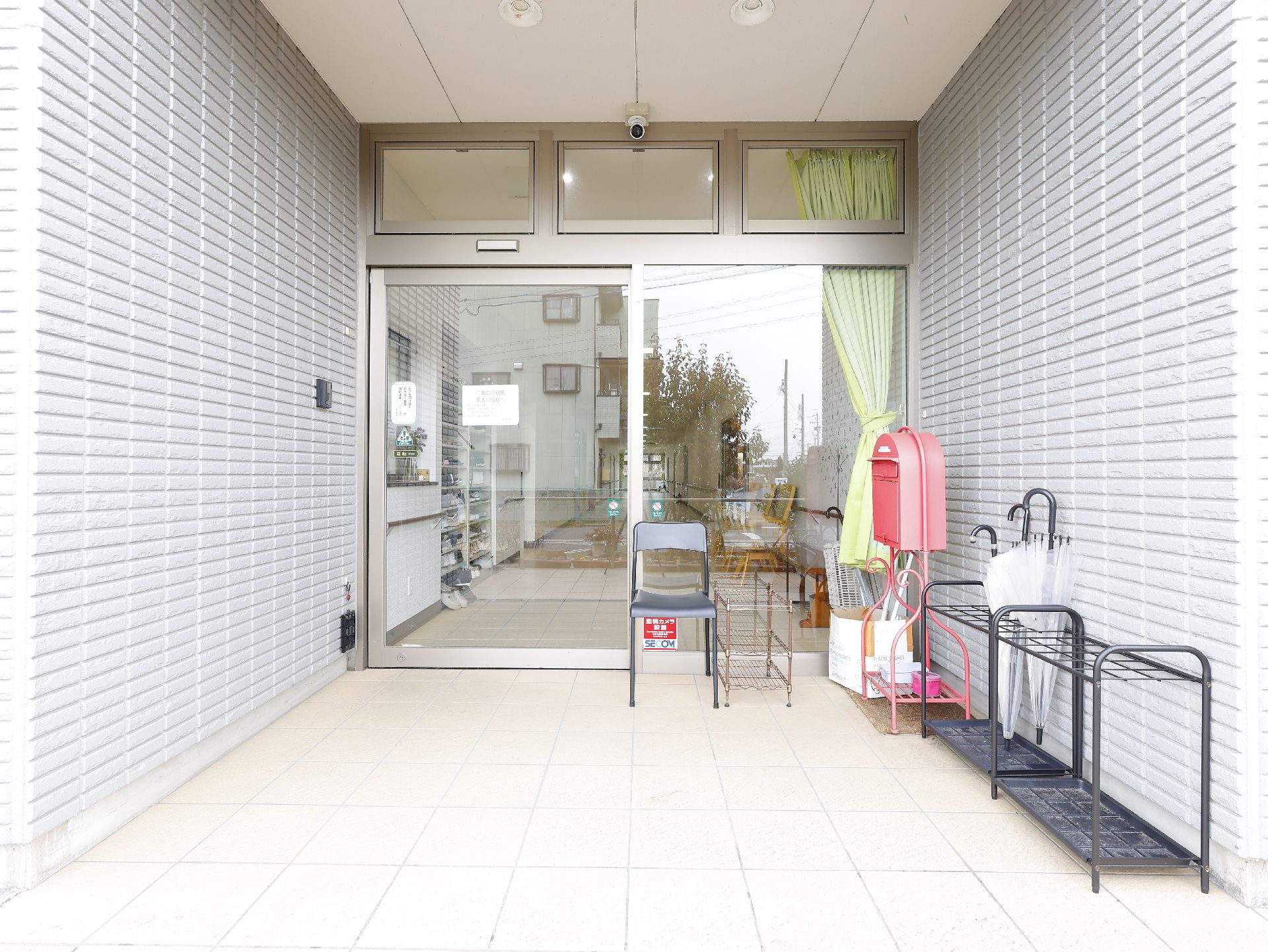 緑の多い屋外で笑顔で散歩をしている車いすの高齢女性と付き添いのエプロンを付けた女性スタッフ。