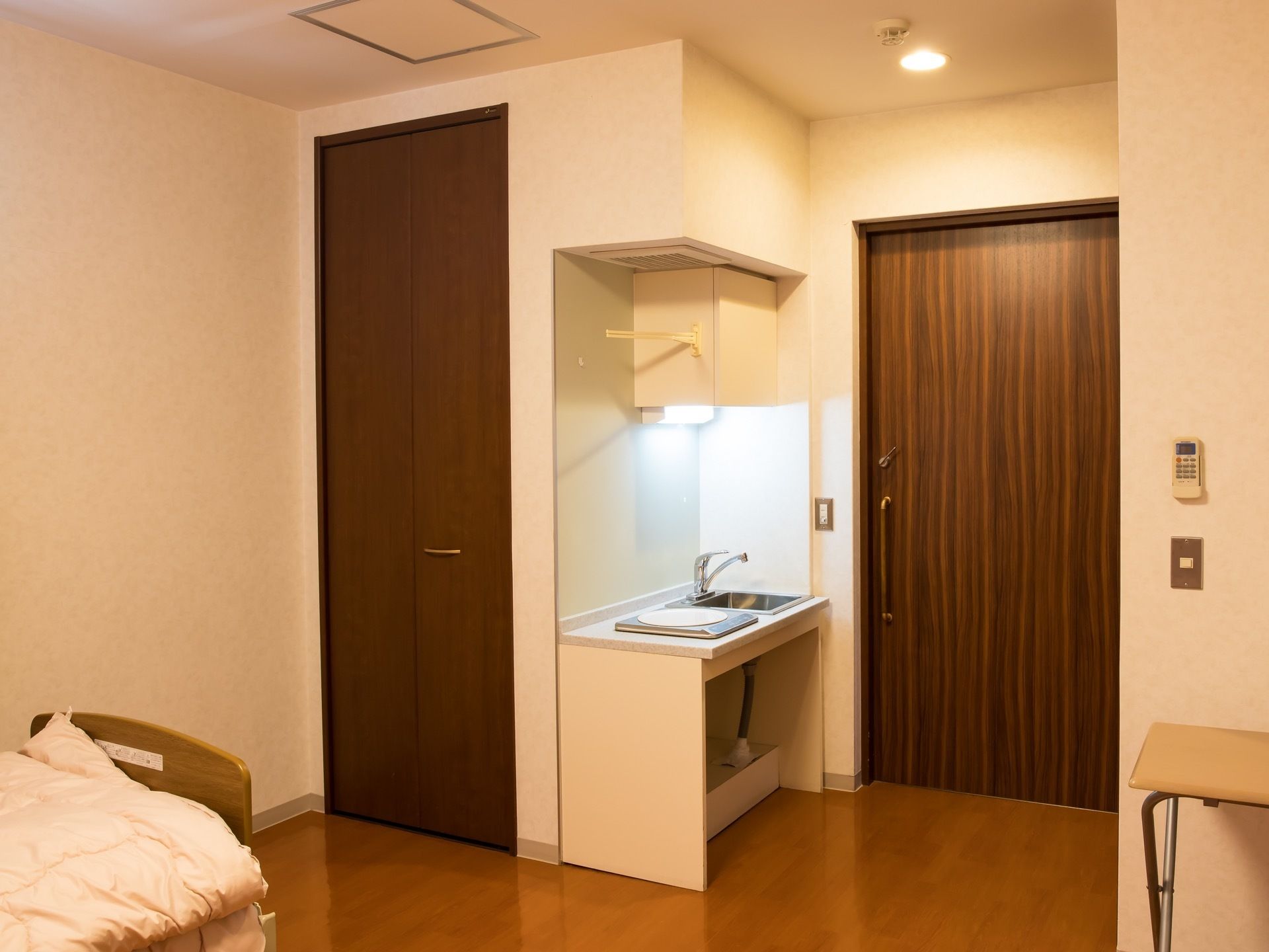 フローリングの部屋にミニキッチンとベッド、備えつけのクローゼットがある。折りたたみ式の机も置かれている。