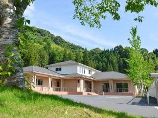 山々に囲まれた施設を外観から写したもの。車いすを押す利用者とスタッフの様子