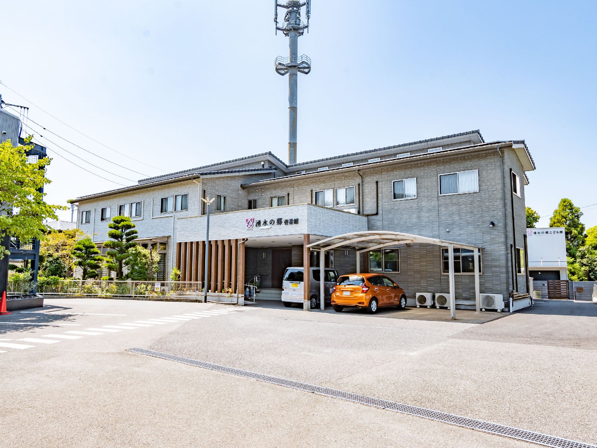 白とオレンジの車が止まっている灰色の外観で２階建ての建物