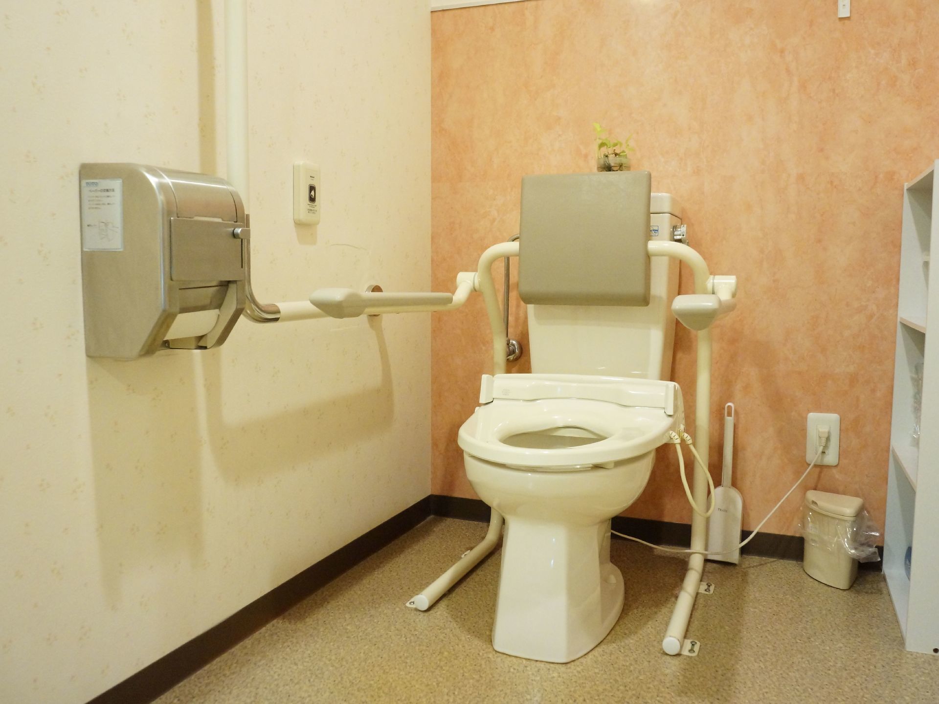 清潔感のあるトイレには真っ白な自動温水便座が完備されている。背もたれになるクッションや手すりも完備され安心である。
